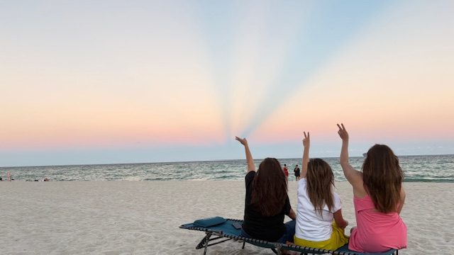 Connie's children at the beach at sunset, raising their hands to the sky
